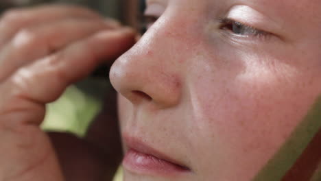 Extreme-Close-Up-of-Girl-Getting-Her-Face-Painted-With-Green-And-Brown-Colors-War-Paint-By-Another-Person