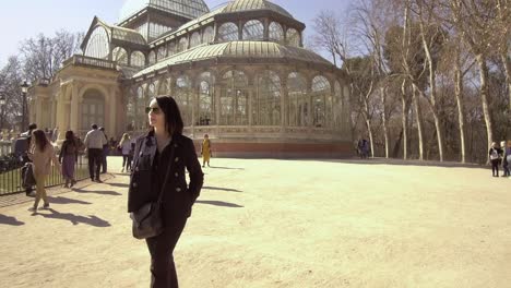 Happy-Female-tourist-in-Madrid,-stroll-outside-Palacio-de-Cristal-in-Retiro-Park,-Madrid