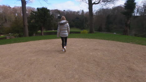 Mujer-Bonita-Rubia-Pasea-Al-Perro-En-El-Parque-Con-Un-Abrigo-Plateado