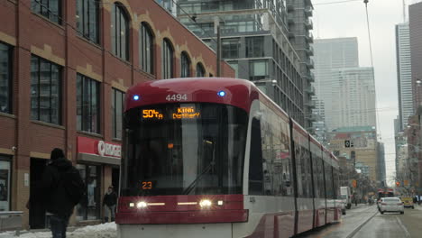 POV-shot-driving-past-a-new-TTC-streetcar-on-King-Street-East-in-Toronto,-with-a-pedestrian-running-across-the-road
