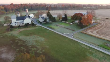 Aerial-flying-overfall-foliage,-the-Conestoga-River-to-an-Amish-Farmhouse,-barn,-silos,-and-fields-Lancaster-County,-Pennsylvania