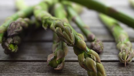 Footage-of-a-bunch-of-fresh,-green-asparagus-falling-on-to-a-wood-table