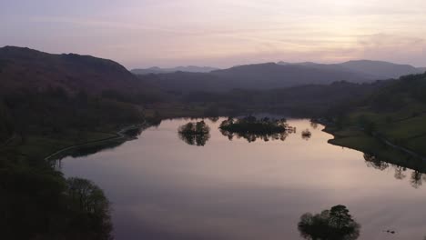 Drone-Parallax-shot-of-a-Lake-at-sunset-with-Mountains-in-the-horizon-in-Keswick-in-The-Lake-District,-Cumbria