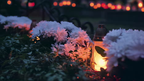 Grab-Mit-Weißen-Blumen,-Die-Von-Einer-Brennenden-Grabkerze-Beleuchtet-Werden