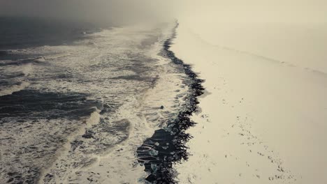 Filmische-Drohnenbewegungen-Zeigen-Einen-Schwarzen-Sandstrand-In-Island,-Der-Von-Einer-Drohne-Bei-Schnee-Gefilmt-Wurde