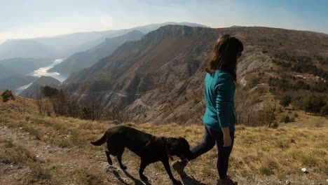 Girl-walking-on-a-mountain-with-a-black-labrador-dog-behind-her