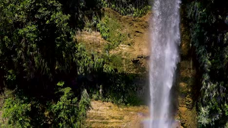 Aerial-shot-panning-down-as-giant-turquoise-waterfall-collects-in-a-pool-below-as-people-relax,-sunbathing---chilling-in-paradise,-tropical-jungle-scenery