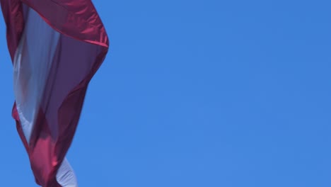 Large-Latvian-flag-waving-slow-on-blue-sky-in-sunny-day,-close-up-shot
