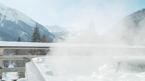 Hot-tub-steaming-and-bubbling-in-the-foreground-with-beautiful-sunny,-snowy-mountains-in-the-background