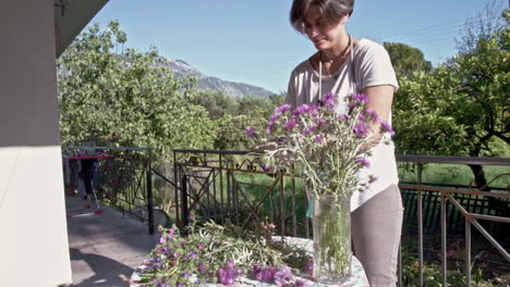 Frau-Schmückt-Eine-Vase-Mit-Wildblumen-Auf-Einer-Veranda-Eines-Landhauses-60fps