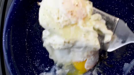 Two-eggs-cooking-in-frying-pan-with-pepper-turned-over-with-spatula-top-view
