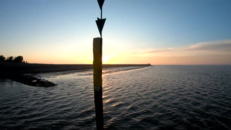 Drone-aerial-footage-birds-eye-view-by-the-ocean-at-the-sunrise-with-a-pole-in-the-middle-of-the-water,-circling-and-orbiting-the-main-subject