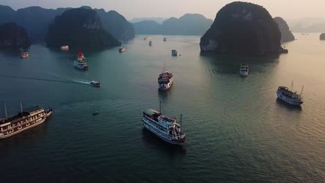 Aerial-shot-moving-slowly-over-ships-in-Ha-Long-Bay-at-dusk,-with-small-boat-moving-towards-foreground