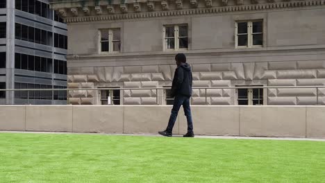 Man-talking-on-phone-and-walking-in-slow-motion-on-top-of-green-roof-in-city