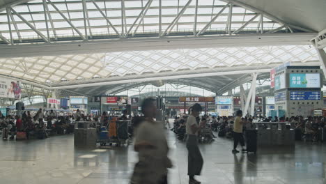 Guangzhou-high-speed-train-South-railway-station-waiting-hall,-with-numerous-passengers-passing-by-and-sitting-on-the-seats,-Guangzhou,-China