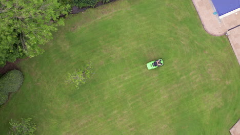Narrow-Rising-Aerial-Shot-of-Man-Mowing-Lawn-of-Home-on-Summer’s-Day-using-Ride-On-Lawnmower-with-Birds-Eye-View-Perspective
