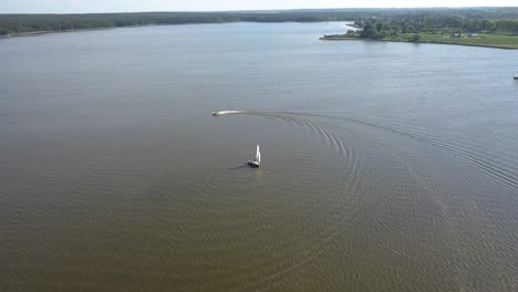 Aerial-tilt-down-shot-of-a-sail-boat-and-a-jet-ski-sailing-on-a-lake-of-Lublin,-Poland