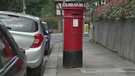 Un-Buzón-De-Correo-Real-Rojo-Con-Un-Coche-De-Correo-Real-Pasando-Por-Una-Calle-Residencial-En-El-Suroeste-De-Londres