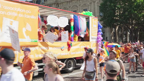 One-of-the-vehicles-transporting-people-that-are-participating-at-the-Gay-Pride-march,-followed-by-the-colorful-crowd-with-swinging-rainbow-flags