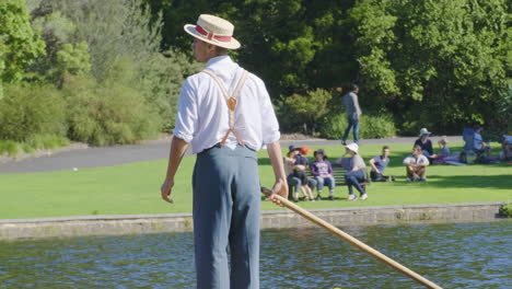 Punt-operator-in-traditional-clothes-rowing-boat-for-guided-tours-of-the-lake-in-the-Botanic-Gardens-Melbourne-Australia