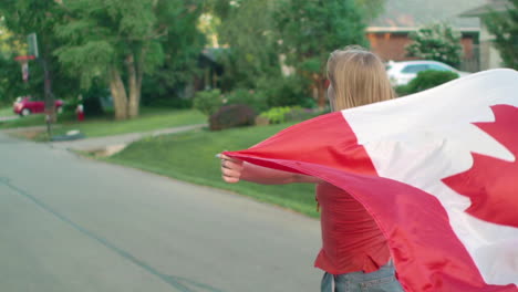 Mädchen,-Das-Auf-Einem-Longboard-Eine-Wohnstraße-Hinunterfährt-Und-Die-Kanadische-Flagge-In-Zeitlupe-Schwenkt