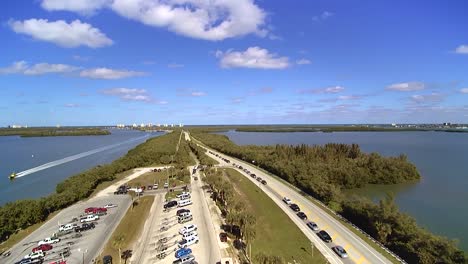 Arial-view-of-the-North-Causeway-off-A1A-in-Ft-Pierce-Florida,-cars-lining-A1A-and-yellow-sea-tow-boat-moving-south-on-the-waterway-at-a-high-rate-of-speed