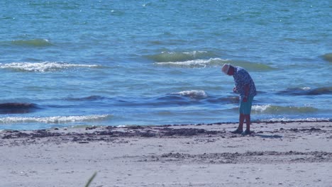 Hombre-Buscando-ámbar-En-La-Costa-Del-Mar-Báltico-En-La-Playa-De-Liepaja-En-Un-Día-Caluroso-Y-Soleado,-Plano-Medio