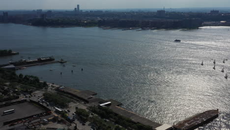 Aerial-tilt-down,-pan-right-by-the-Hudson-River,-boats,-traffic-in-New-York-with-New-Jersey-in-the-background---a-few-boats-in-the-calm-waters