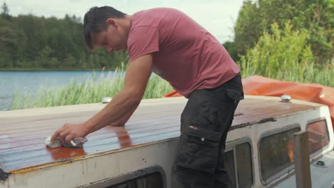Young-man-wiping-dust-off-boat-roof-planking-after-sanding-planking