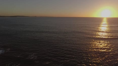 Sunrise-drone-shot-over-water-with-sun-at-right-of-frame