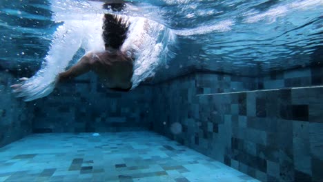 Unterwasseraufnahme-In-Extremer-Zeitlupe-Eines-Mannes,-Der-Rückwärts-In-Den-Pool-Fällt-Und-Eine-Gopro-Kamera-Hält