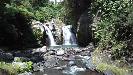 Drohnenschuss,-Der-Rückwärts-Von-Einem-Der-Alingaling-Wasserfälle-In-Bali,-Indonesien,-Wegfliegt,-Während-Touristen-Herumlaufen-Können