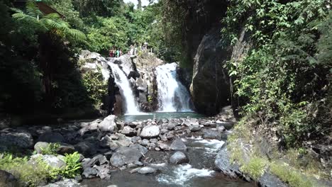 Drone-Shot-flying-backwards-away-from-one-of-the-AlingAling-Waterfalls-in-Bali,-Indonesia-while-tourists-can-be-seen-walking-around