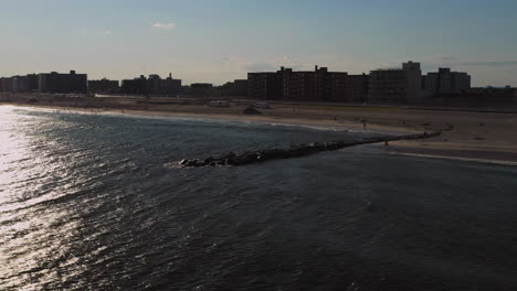 low-fast-drone-pan-left-over-the-ocean,-facing-the-shore-in-Long-Beach,-New-York