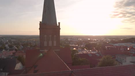 A-Point-of-interrest-aerial-drone-shot-of-a-red-brick-church-of-in-a-little-town-in-northern-Germany,-while-flying-in-golden-hour,-vertigo-effect