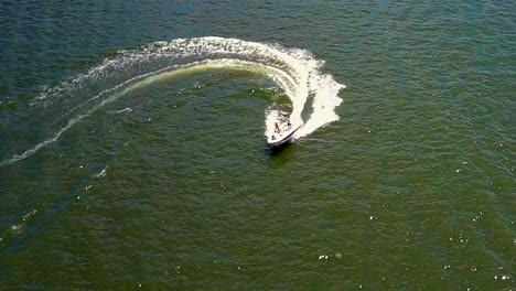Pull-back-aerial-drone-shot,-of-boat-in-Big-Bear-Lake,-going-back-for-person-that-was-water-skiing
