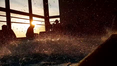 Silhouettes-of-people-at-indoor-pool-party-at-sunset,-water-splashing-in-slow-motion,-static-low-angle