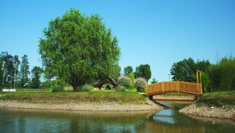Island-in-pond-with-wooden-bridge-across-water-with-small-hut,-exterior-design-and-landscaping
