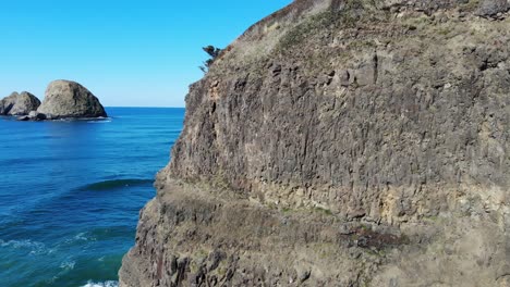 Drone-flies-sideways-near-a-cliff-revealing-sea-stacks-behind-in-the-ocean