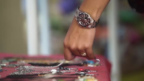 day-shot-close-up-of-female-hand-choosing-jewelry-from-street-flea-market-hand-with-clock-and-silver-ring-,-some-bracelets-on-table