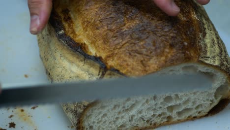 Chef-slicing-fresh-sourdough-loaf-in-cafe-kitchen,-closeup