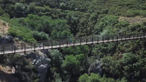 Drone-Shot-following-an-active-man-running-on-an-outdoor-hanging-suspension-bridge-above-Bear-Canyon-in-Draper-City,-Utah