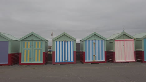 Breite-Aufnahme-Von-Bunten-Strandhütten-Am-Strand-Von-Brighton,-Mit-Einer-Läuferin,-Die-Vorbeiläuft