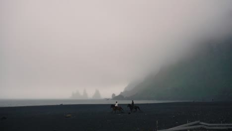Horses-running-in-SlowMotion-across-black-sand-beach,-in-a-foggy-day-in-Vik,-Iceland