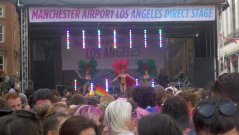 Leeds-Pride-LGBTQ-Festival-2019-shot-of-the-crowd-in-foreground-dancing-and-waving-flags-with-drag-queens-on-the-stage-dancing-close-up-focused-on-crowd-4K-25p