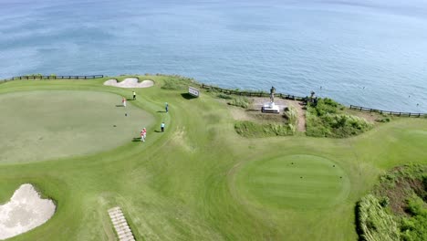 Female-players-at-New-Kuta-Golf-Course-near-ocean-cliff-and-golfer-statue,-Aerial-orbit-around-shot
