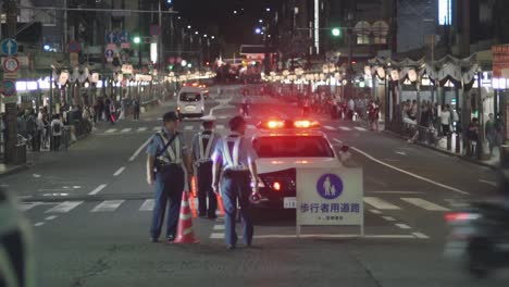 Japanese-Policemen-Directing-Traffic-With-A-Road-Block-During-The-Yoiyama-Festival-At-The-Gion-Matsuri-Festival-In-Kyoto,-Japan-At-Night