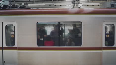 Pasajeros-En-El-Vagón-De-Tren-Ven-A-Través-De-La-Ventana-De-Vidrio-En-Tokio,-Japón