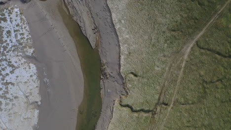Aerial-rising-top-down-shot,-of-the-sandy-trenches-at-the-shoreline-at-low-tide