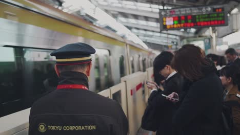 Japanisches-Zugpersonal-Steht-Auf-Dem-Bahnsteig-Mit-Passagieren-Auf-Dem-Bahnsteig,-Während-Sich-Der-Zug-Dem-Tokio-bahnhof-In-Japan-Nähert